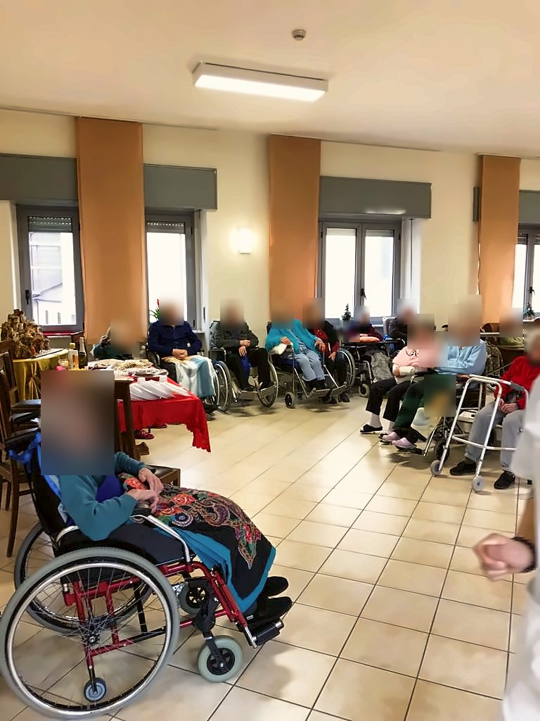 Ospiti riuniti nel salone attorno a una tavola imbandita per una festa; i volti sono oscurati