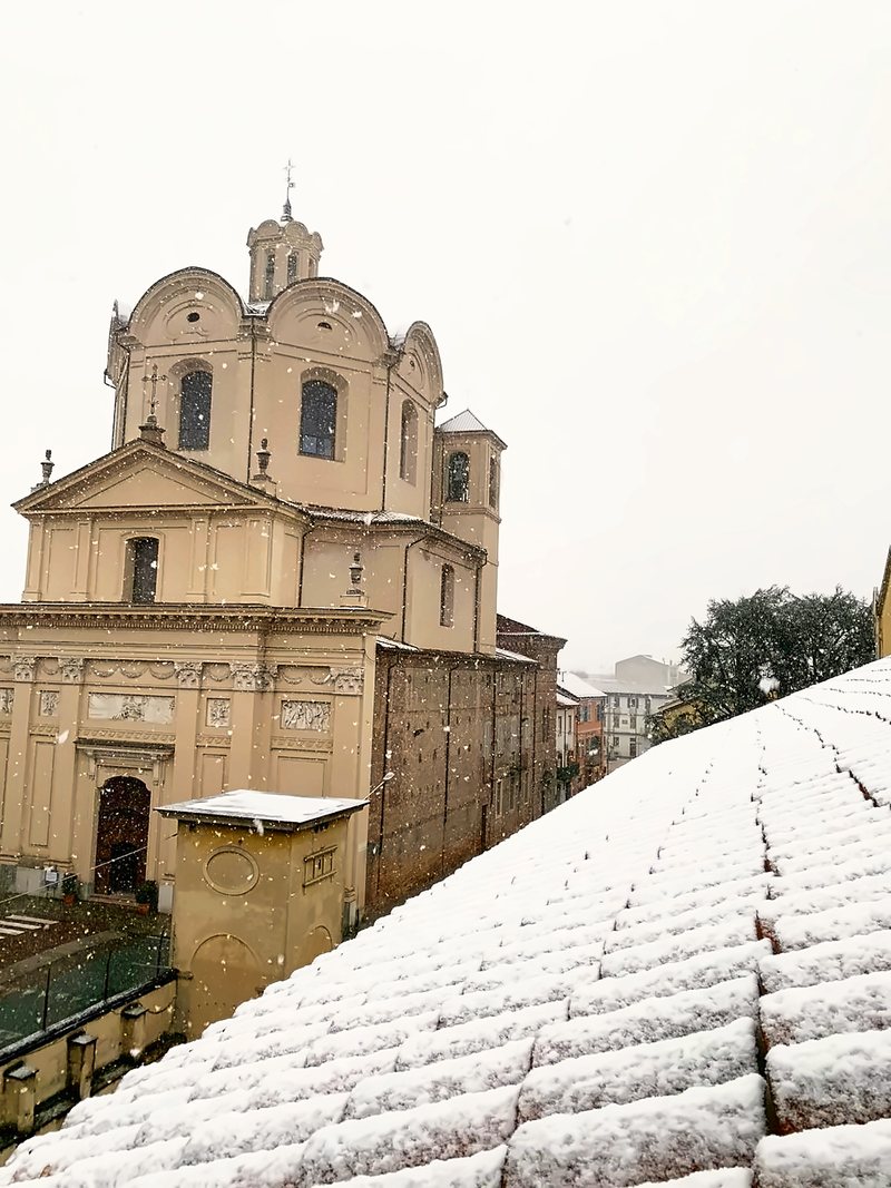 Tetti innevati e la facciata di una chiesa del centro storico sotto la neve